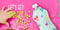 Child's hand near a colorful heart-patterned baby food pouch with scattered snacks on a pink mat.
